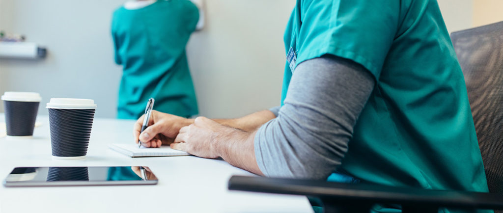 2 nurses sit and write while drinking coffee