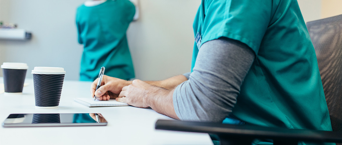 2 nurses sit and write while drinking coffee