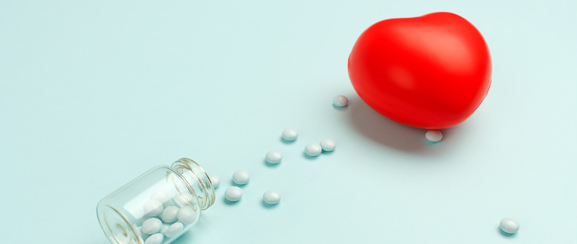 Bottle of white pills spilled out on the table with a heart shaped stress ball