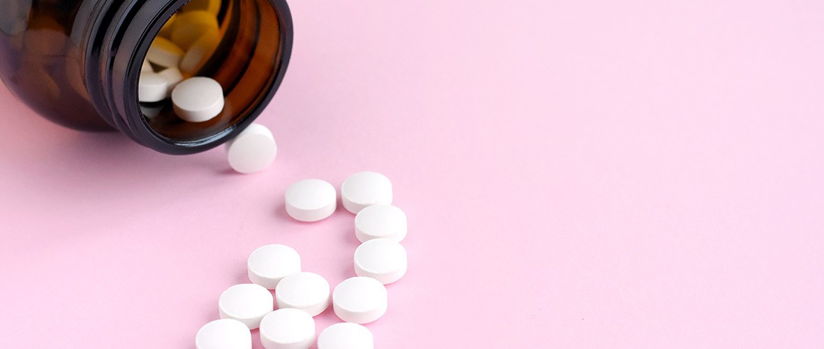 Bottle of small white pills spilled out on a pink surface