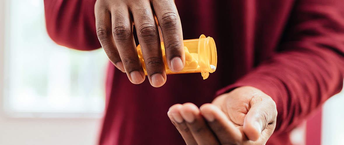 A man shakes white pills into his hand