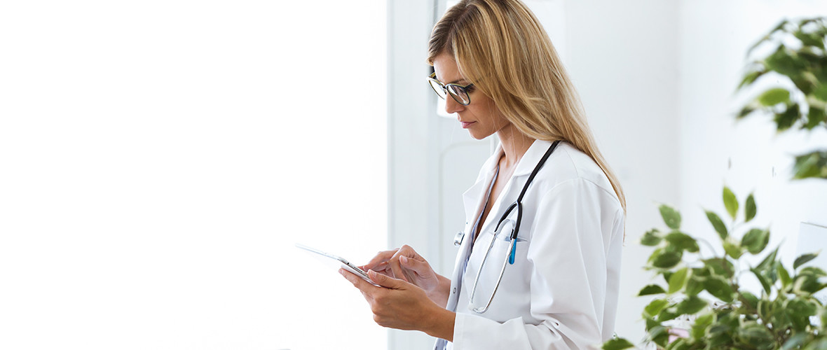 A doctor is standing using a mobile tablet