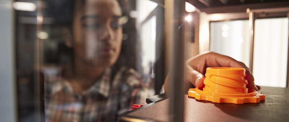 Girl reaching into a machine and holding an orange, gear-shaped part