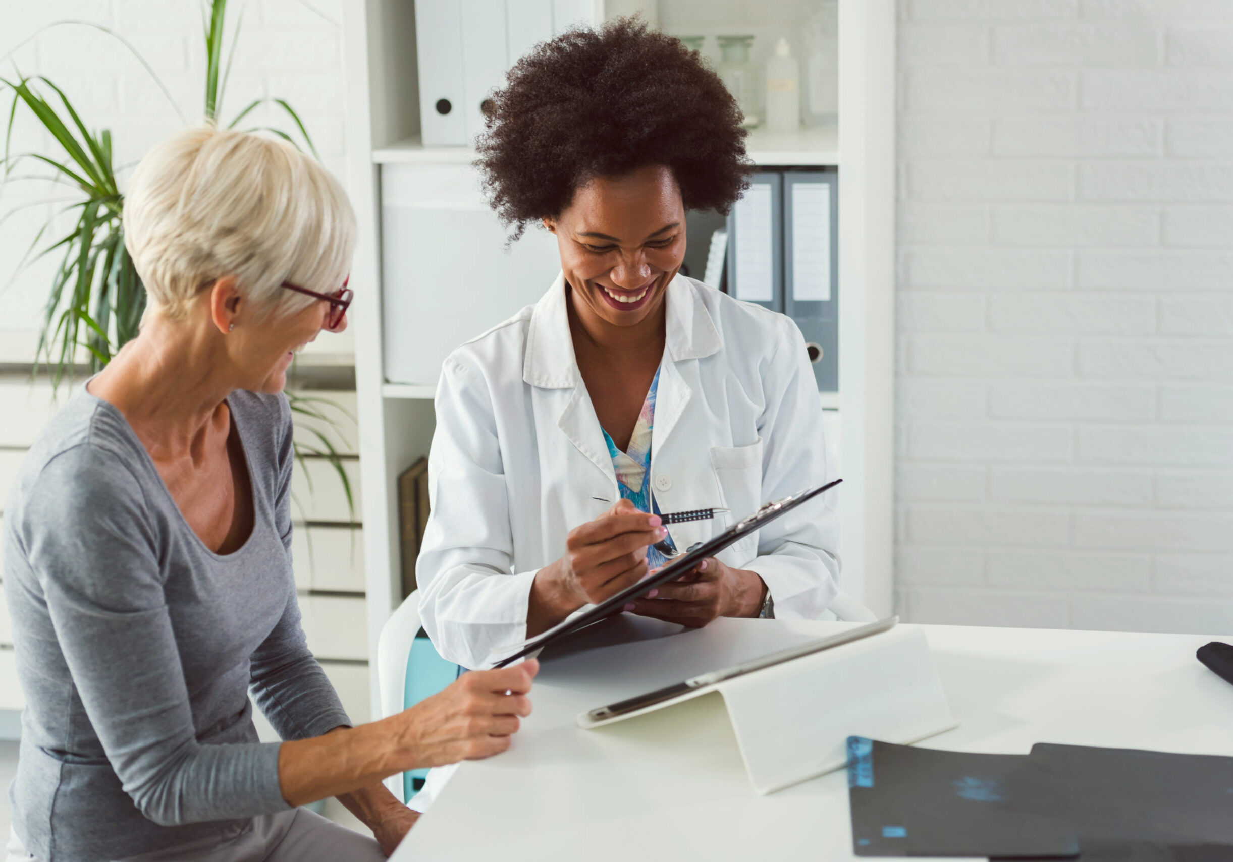 A female doctor sits at her desk and chats to an elderly female patient while looking at her  test results