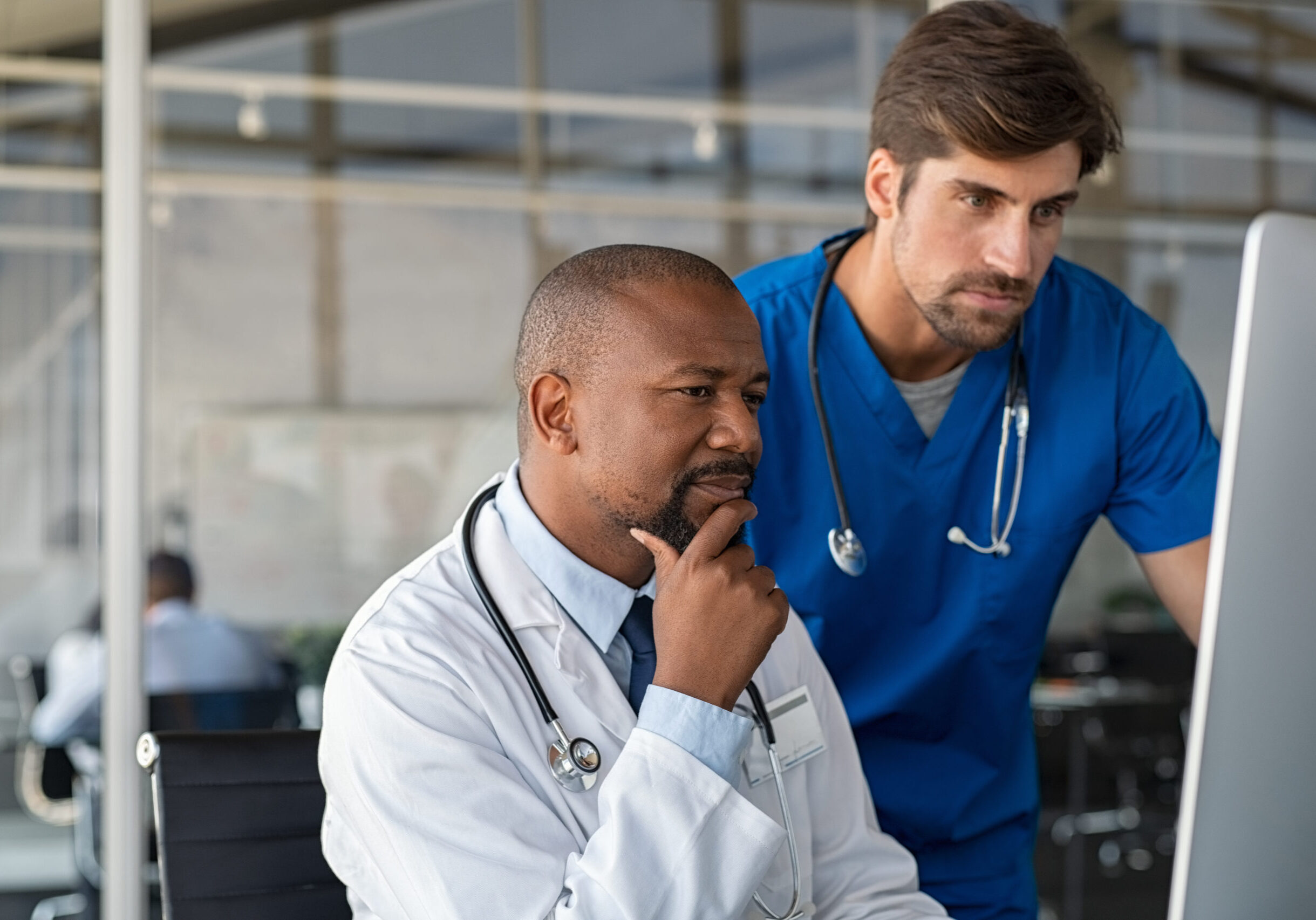 Mature african doctor and nurse analyze medical report on computer in office. Two healthcare workers in consultation using computer at hospital. Doctor discussing medical report with colleague at clinic.