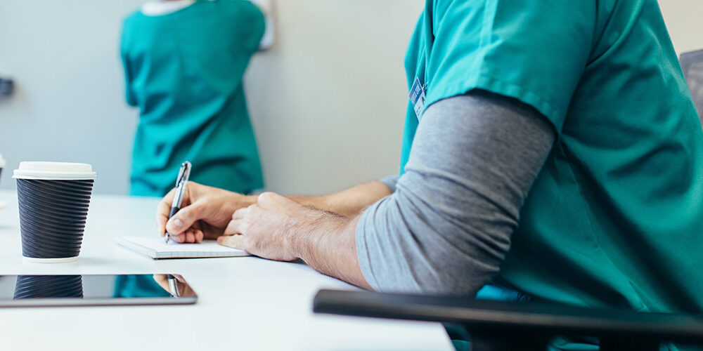 2 nurses sit and write while drinking coffee