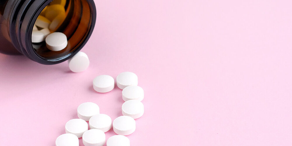 Bottle of small white pills spilled out on a pink surface