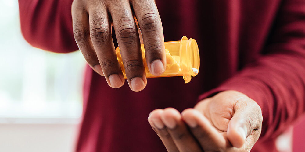 A man shakes white pills into his hand