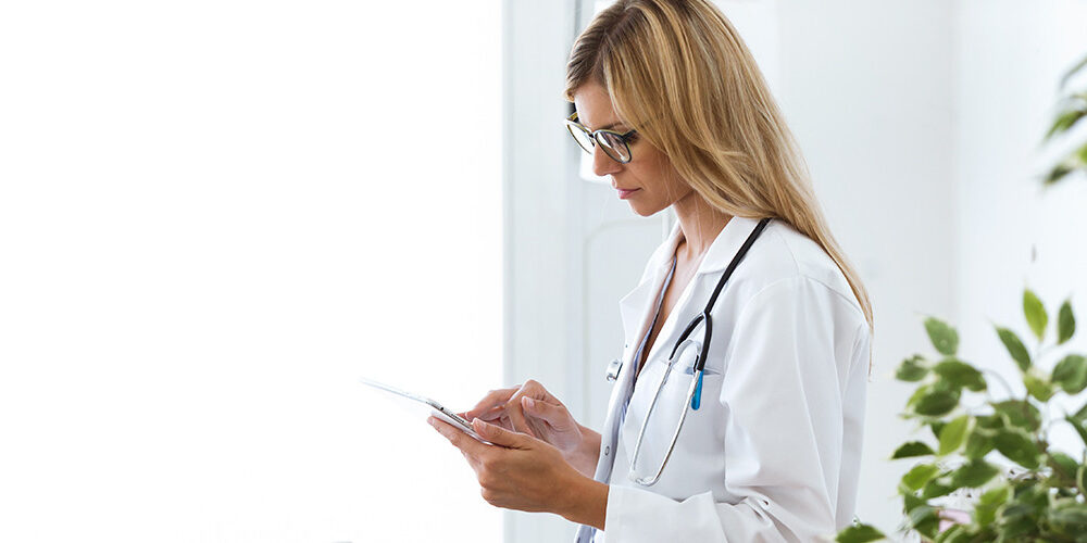 A doctor is standing using a mobile tablet