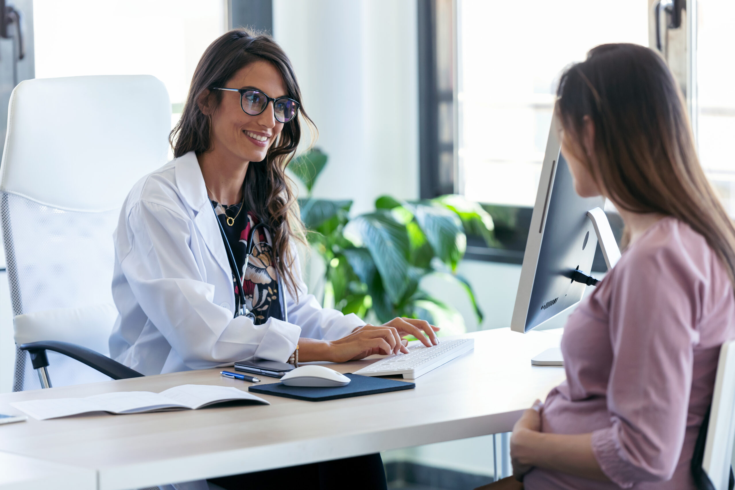 Shot of pretty young woman gynecologist reviewing the medical history of her pregnant patient with computer in the clinic.